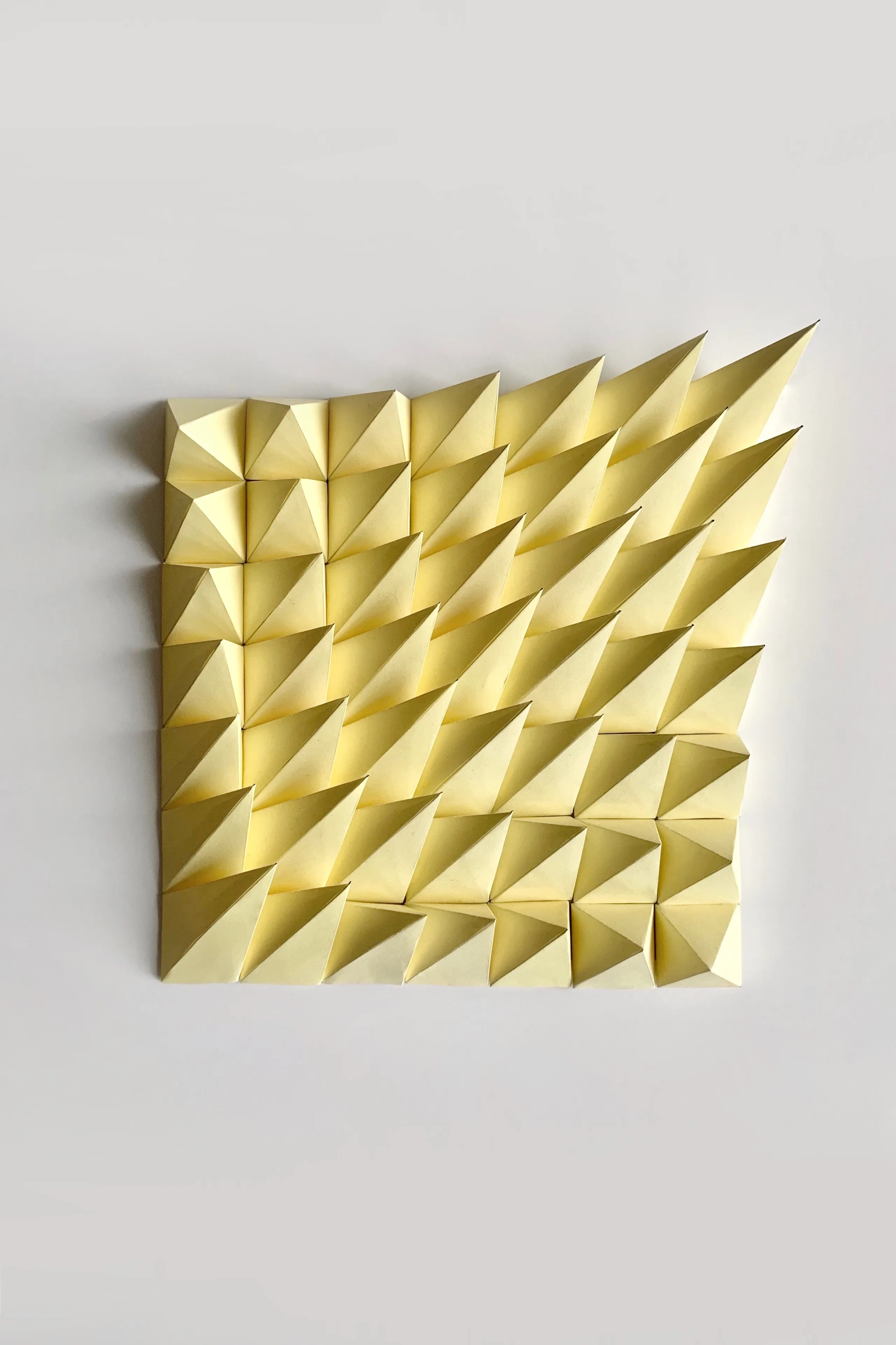 The yellow paper relief head-on against a white wall, 49 pyramid tips in a square grid