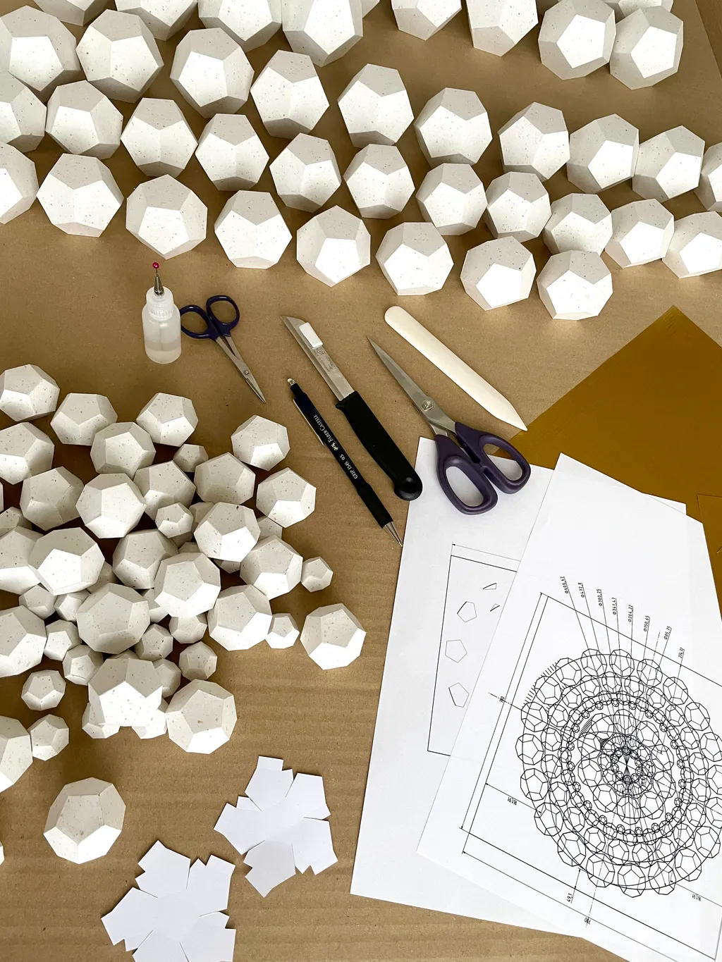 Big Art Show 2026 – Dozens of white dodecahedra on the worktable, beside them tools and the technical drawing of the ring pattern