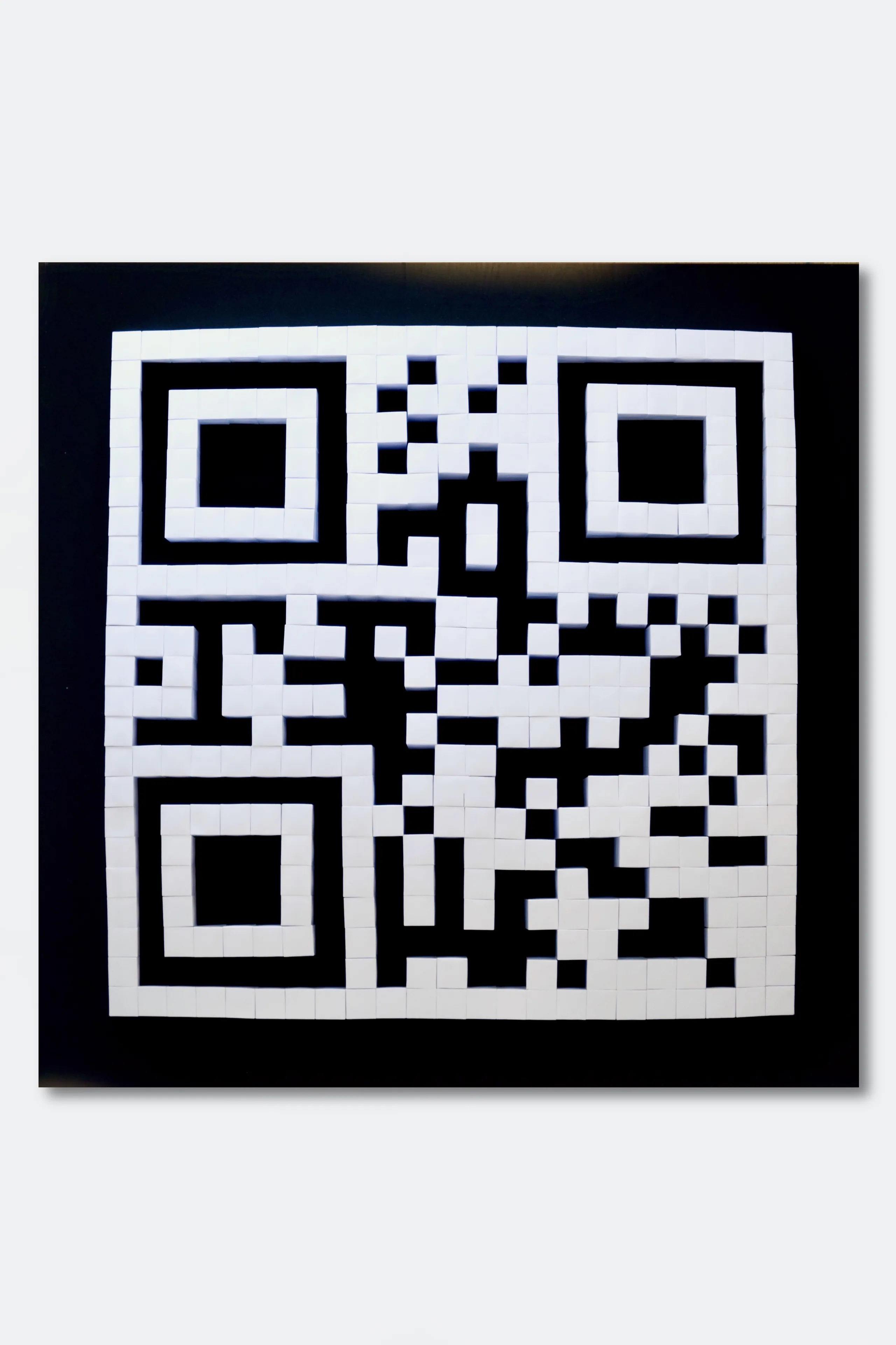 A QR code built from white paper prisms on a black ground, seen head-on and fully readable