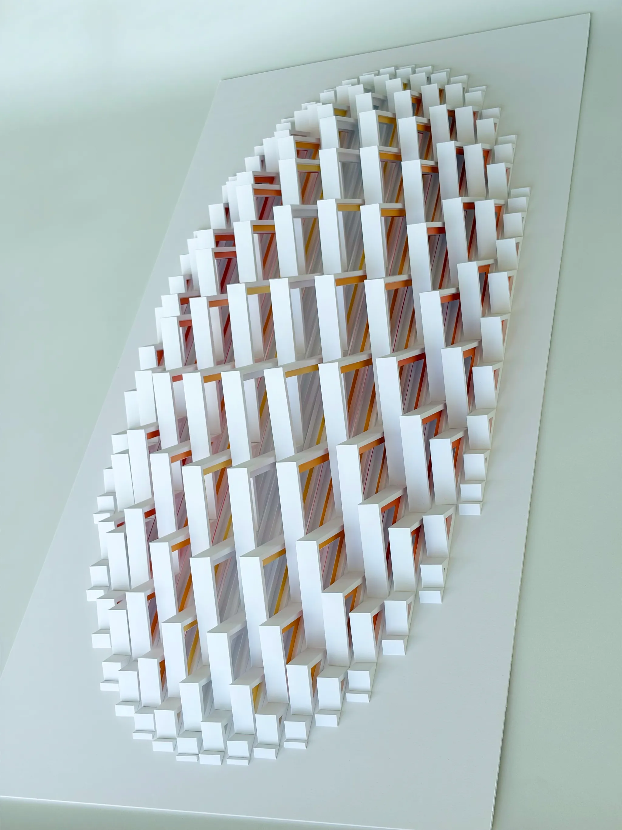 No. 24 – Triangula – The whole work at an angle from above on its white board, yellow and orange edges glowing between the modules