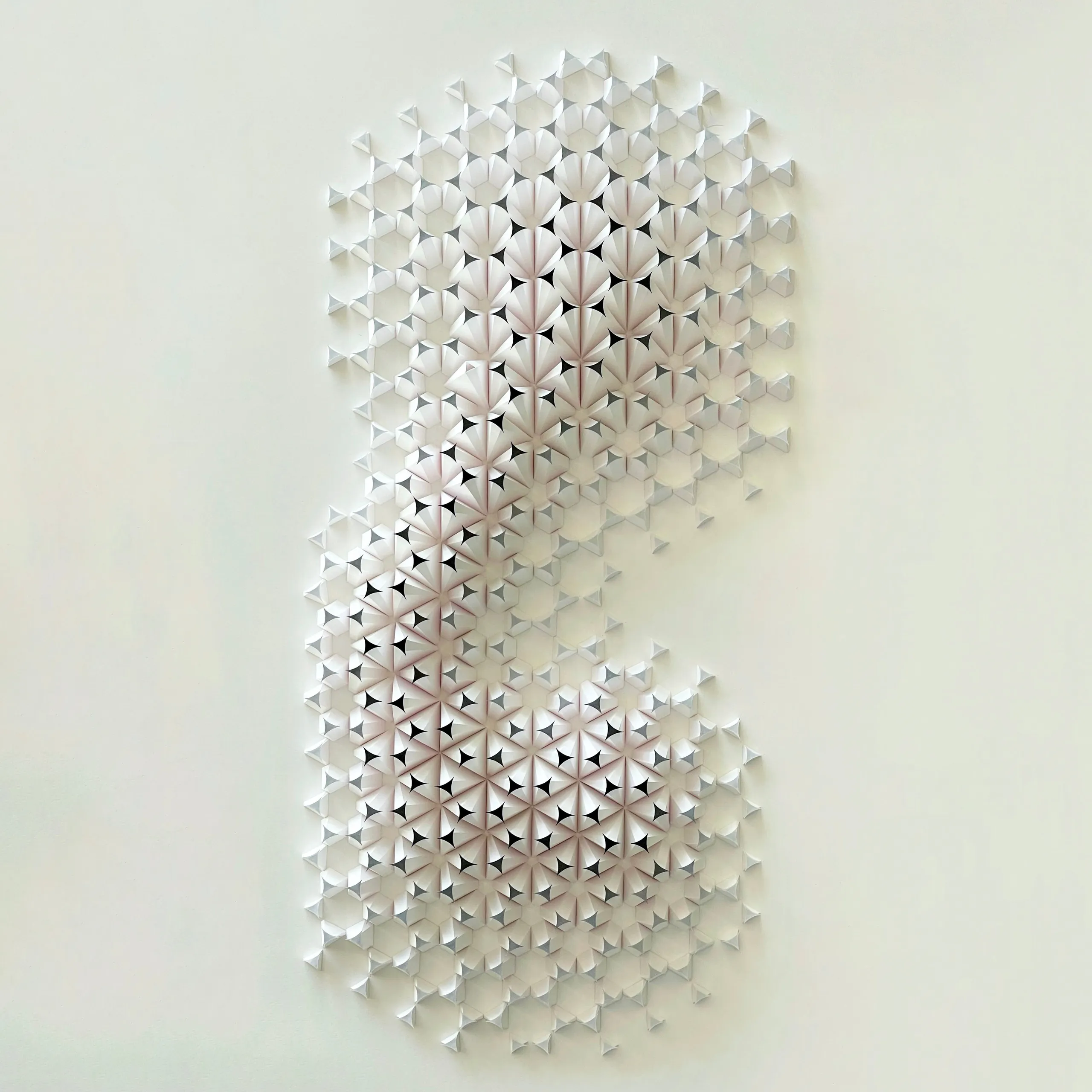 The whole work head-on, an S-shaped swarm of white paper fans on a hexagonal grid