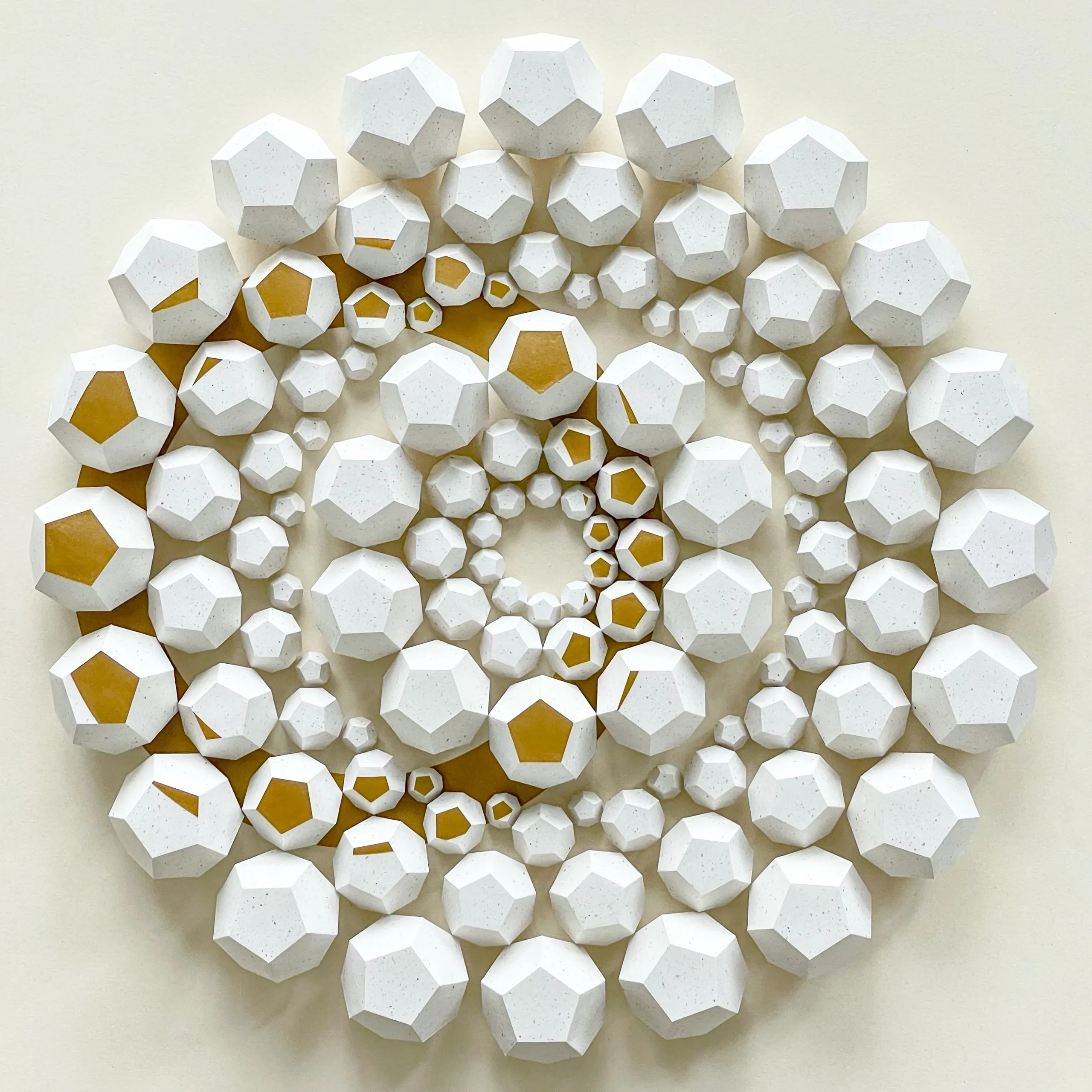 The whole work head-on, concentric rings of white dodecahedra with single faces in gold