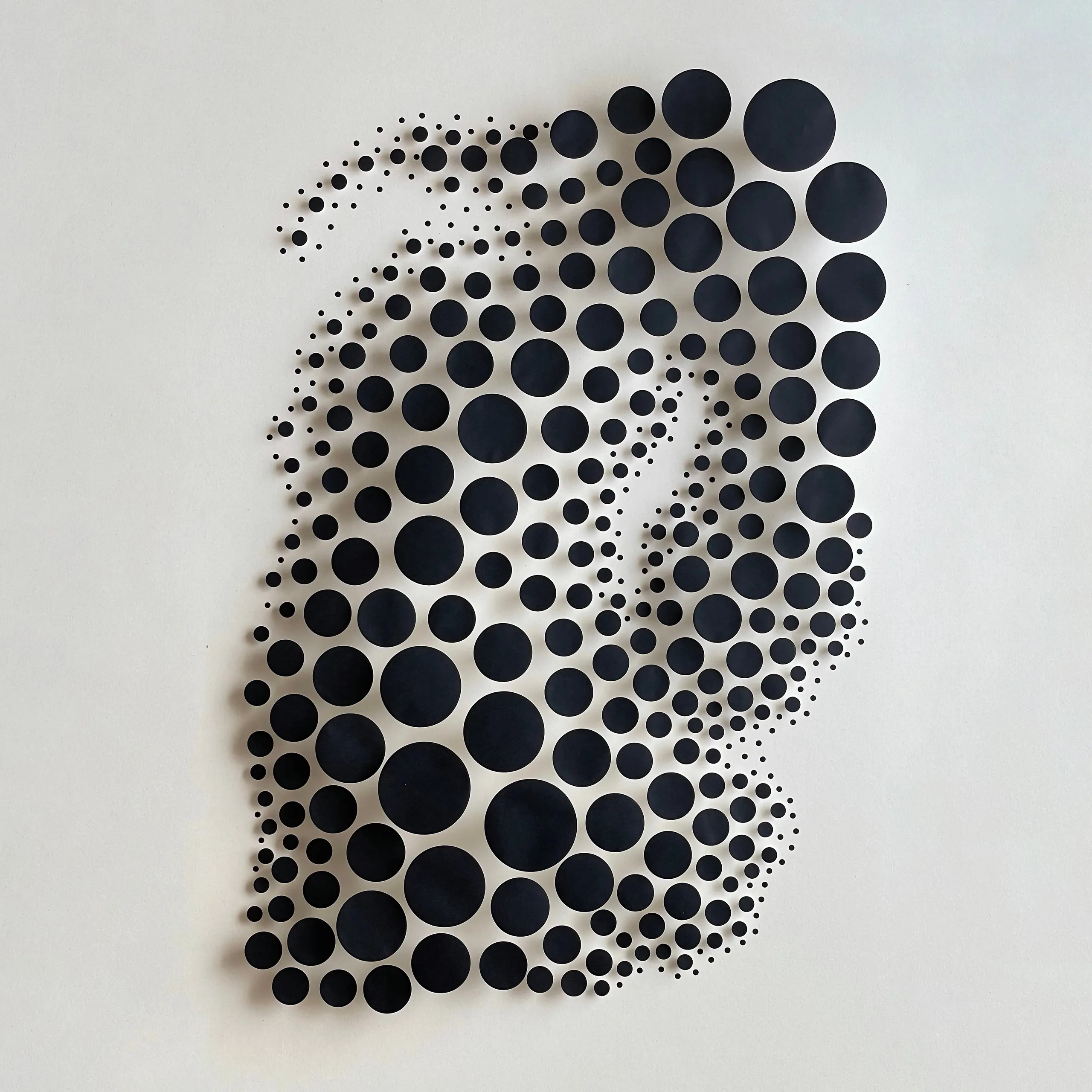 The whole work head-on, black circles of varying size hovering above a beige ground as a swarm