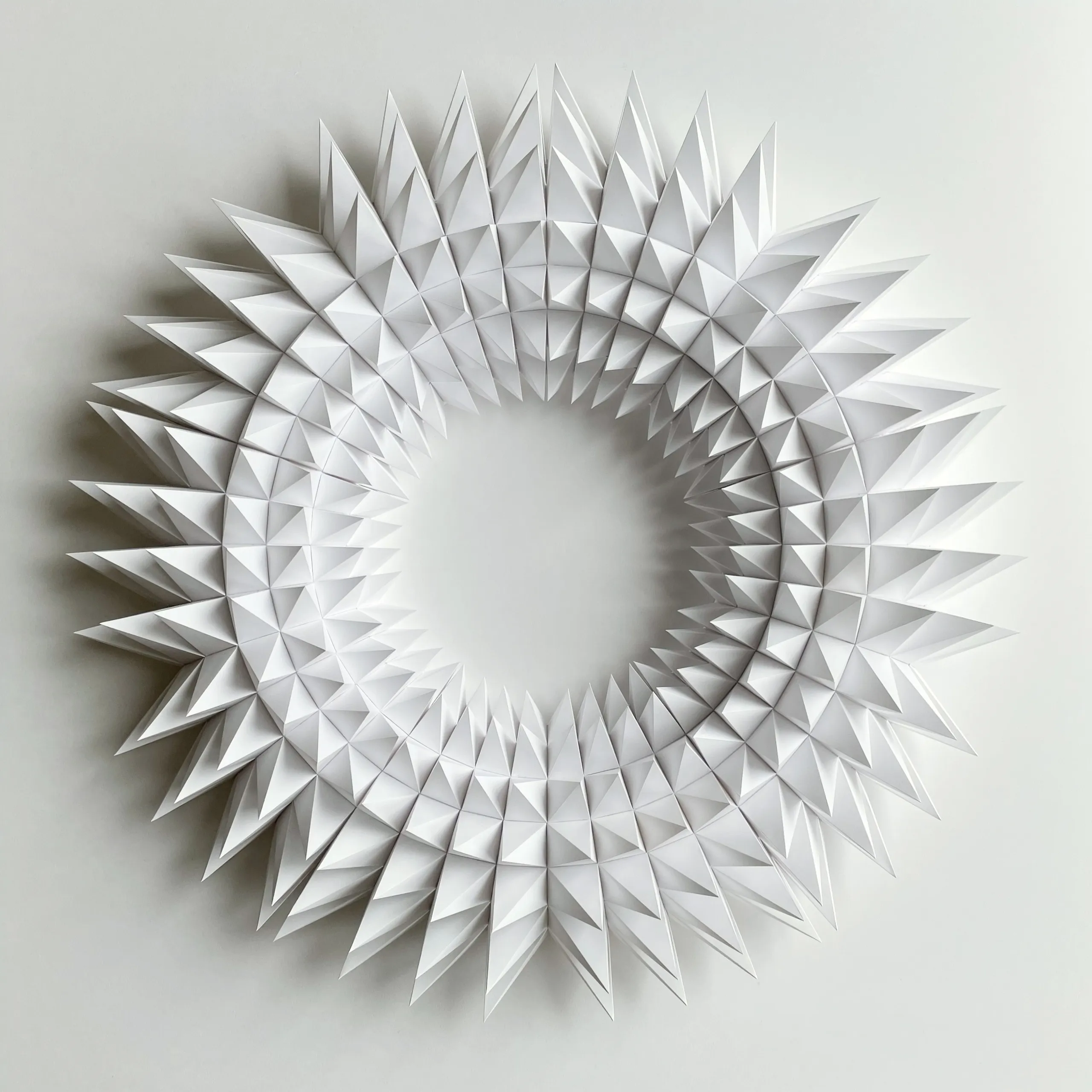 The whole work head-on, a white wreath of pyramid tips in three rings around an empty centre