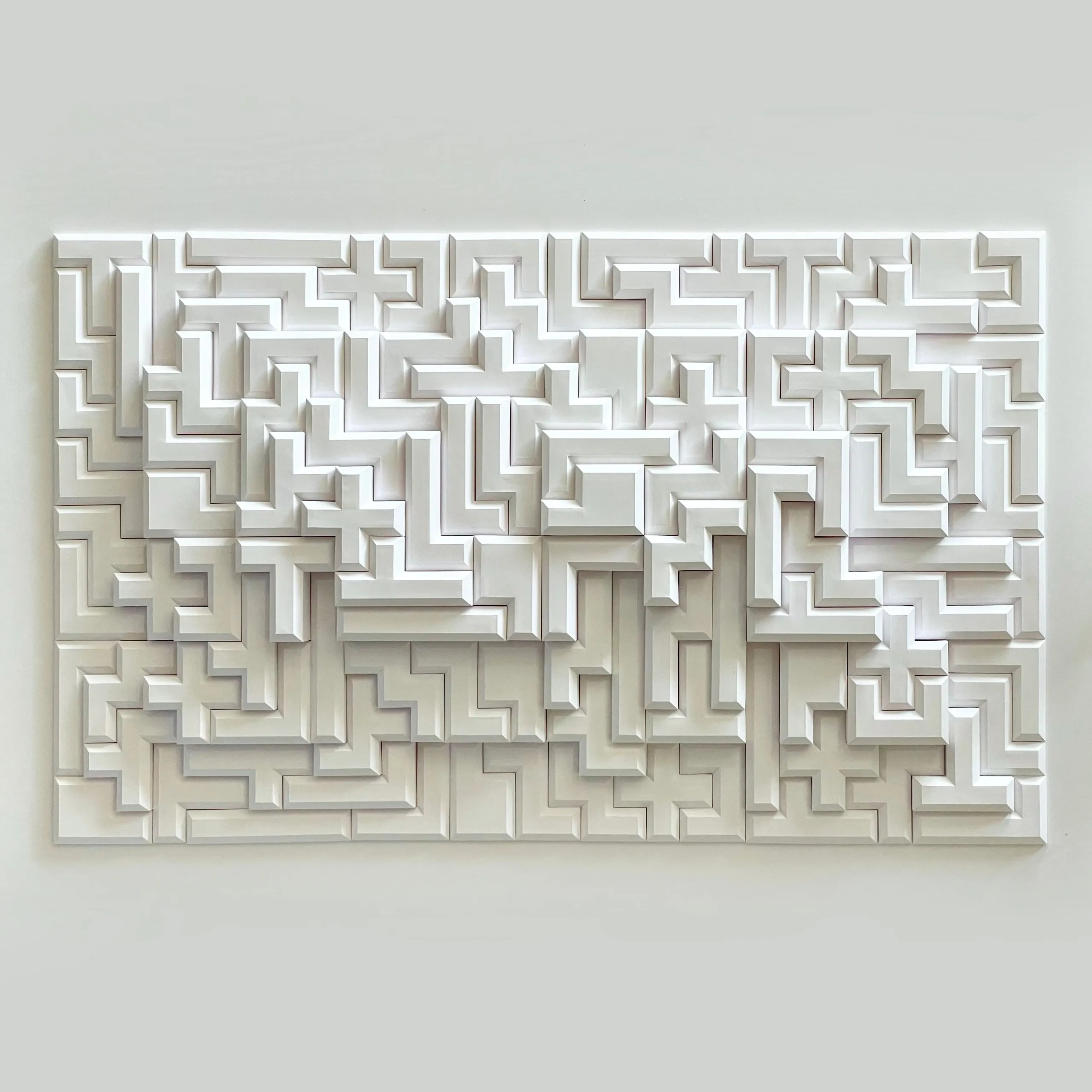 The whole white relief head-on, a hundred interlocking pentomino pieces forming a labyrinth-like grid