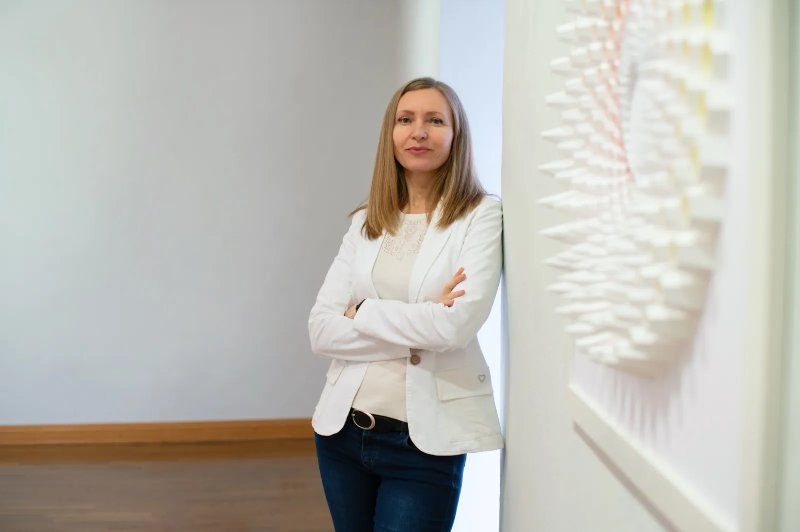 Larisa Semke neben einem ihrer weißen Wandreliefs aus gefaltetem Papier