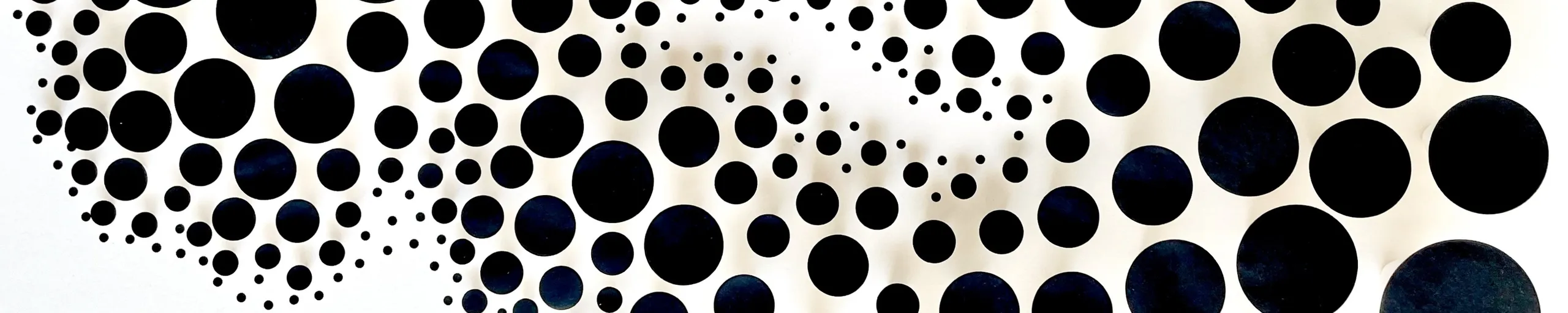 The black discs floating just above the beige ground, their shadows lying beneath as a second pattern